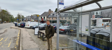 Andrew Bowie MP standing beside a bus stop in Aboyne.