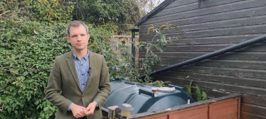 Andrew Bowie MP standing beside a heating oil tank.